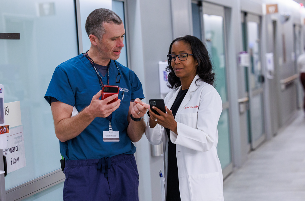 Dr. Raina Merchant (in white coat) and Dr. Bryan Walker Lee look at their mobile phones.